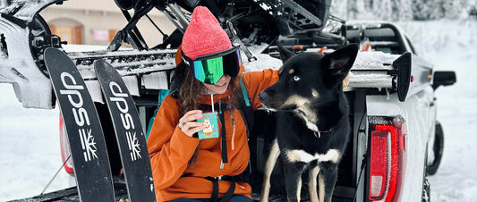 A woman sat with her dog, on a truck in the snow